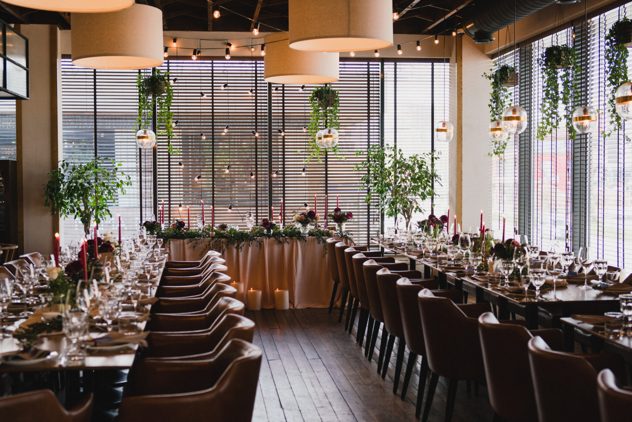 Coziness and style. Modern event design. Table setting at wedding reception. Floral compositions with beautiful ranunculus flowers and greenery, candles, laying and plates on decorated table.